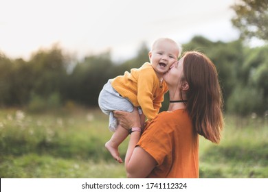 Caucasian mother holding baby walks in deserted places, mom in linen dress holds one-year-old baby in her arms, walking in park, concept of motherhood and summer, social distance from other people