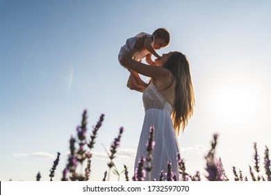 Caucasian Mother Lifting Her Child Under Sunset. Silhouette Of Mother And Son At Sunset. Family Having Fun Together Outdoors. Motherhood Concept.