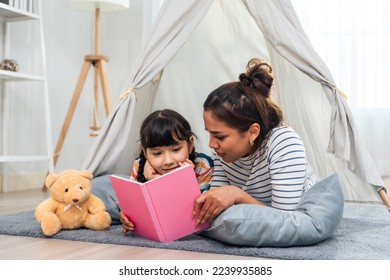 Caucasian mother read story and telling a fairy tale to young daughter. Happy family, Beautiful mom lying down in decorated tent and playing with adorble cute girl during holiday weekend in house.