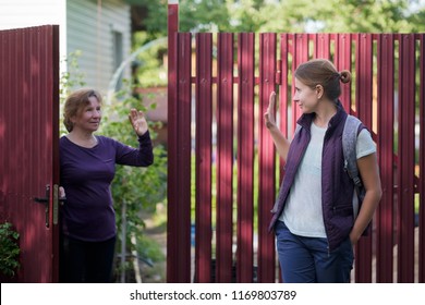 Caucasian Mother Saying Goodbye To Her Daughter As She Are Leaving. They Are Standing Near Red Fence Of Country House