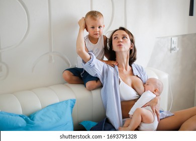 Caucasian mother with two children on the bed at home, mother breastfeeds the baby and the eldest son plays and jumps nearby. stay home