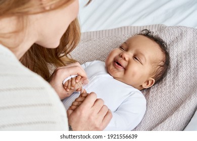 Caucasian mum, foster single parent holding hands of happy cute adorable adopted infant african american baby girl daughter lying on bed. Child care, diverse ethnicity mother and child concept.
