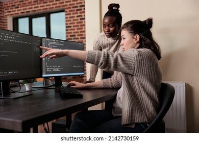 Caucasian network developer pointing out high usage of processing power in mainframe grid. African american programmer helping coworker to solve overloaded system storage space.