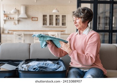 Caucasian old elderly senior woman packing sorting her clothes items stuff shirts in a bag suitcase luggage baggage for traveling abroad, moving to another place house home - Powered by Shutterstock