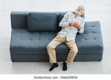 Caucasian Old Senior Elderly Gray Hair And Bearded Man Lying Down Close Eyes On Sofa In Living Room At Home Alone Holding Hands On Chest Suffering From Sudden Problem Painful Emergency Heart Attack.