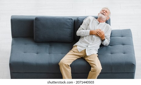 Caucasian Old Senior Elderly Gray Hair And Bearded Man Lying Down Close Eyes On Sofa In Living Room At Home Alone Holding Hands On Chest Suffering From Sudden Problem Painful Emergency Heart Attack.