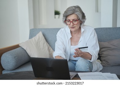 Caucasian Older Woman In Eyewear Using A Credit Card And A Laptop To Purchase Online. Mature Elderly Retired Female Shopping On The Internet. E-banking Is Available Immediately By The Elderly.