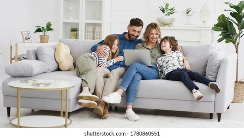 Caucasian parents with kids on couch using gadget. Young man and woman with son and daughter spending time together with laptop. Father and mother watching something online on computer. Rest at home.