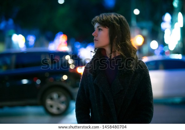 Caucasian\
pedestrian woman walking the street at night in the city with\
moving cars in the background.  She looks nervous or unsure like a\
lost tourist or afraid of commuting alone.\
