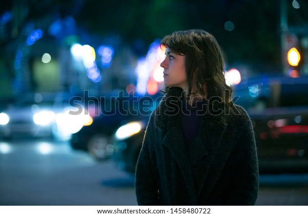 Caucasian\
pedestrian woman walking the street at night in the city with\
moving cars in the background.  She looks nervous or unsure like a\
lost tourist or afraid of commuting alone.\
