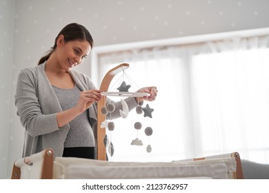 Caucasian Pregnant Woman Installing A Baby Mobile Toy Over The Baby's Crib