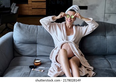 Caucasian pregnant woman sitting on a sofa and putting cucumber slices on her face. Concept of pregnancy and natural self-care. - Powered by Shutterstock