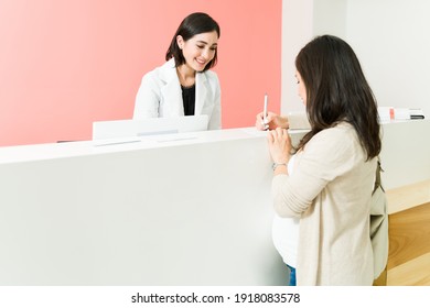 Caucasian pregnant woman writing and checking herself in at the reception desk of her gynecologist doctor 
