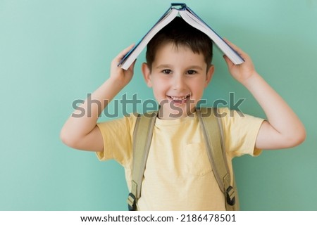 Caucasian preschool boy with school backpack holds book on a light green background with copy space