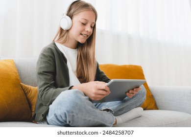 Caucasian preteen schoolgirl pupil daughter using digital tablet for watching movies, listening to the music in headphones, surfing social media, e-learning online from home. - Powered by Shutterstock