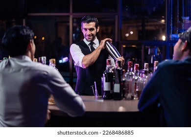 Caucasian profession bartender making a cocktail for women at a bar. Attractive barman pouring mixes liquor ingredients cocktail drink from cocktail shaker into the glass at night club restaurant.