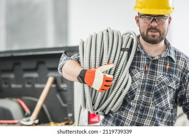 Caucasian Professional Contractor with Conduit Electric Pipe on His Shoulder. Men Wearing Eyes Protection Glasses and a Hard Hat.