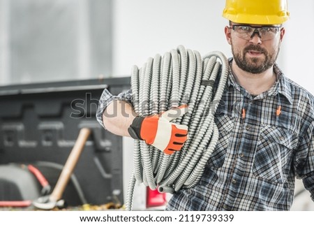 Caucasian Professional Contractor with Conduit Electric Pipe on His Shoulder. Men Wearing Eyes Protection Glasses and a Hard Hat.