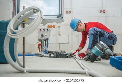 Caucasian Professional Electrician at Work. Electric Cables Plastic Pipe Conduit Installation Inside Newly Constructed House. 
