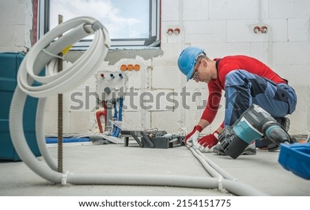 Caucasian Professional Electrician at Work. Electric Cables Plastic Pipe Conduit Installation Inside Newly Constructed House. 