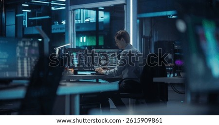 Caucasian Quantum Computer Engineer Working in a Dark Office in an Advanced Computer Research and Development Facility. Young Male Programming the Work and Data Flow of a Quantum Computer