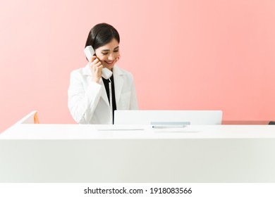 Caucasian Receptionist Smiling While Talking On The Phone With A Patient. Female Worker Making A Medical Appointment At The Reception Desk