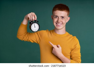 Caucasian Red Head Boy Holding Alarm Clock And Pointing At It