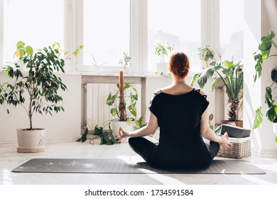 Caucasian Redhair Woman Practice Yoga At Home In A White Light Living Room. Window And Plants Background