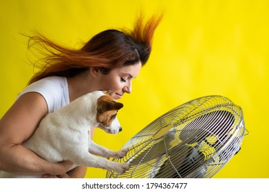 Caucasian Red-haired Woman And Dog Cool Down Near An Electric Fan.