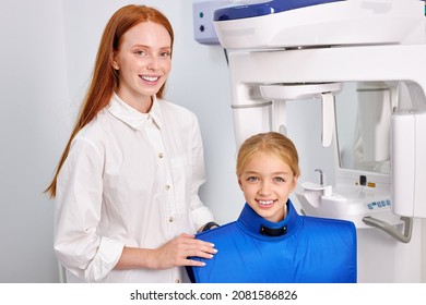 Caucasian Redhead Female Dental Specialist Is Going To Examine An X-ray Of Child Girl In Modern Dental Clinic By Professional Specialist. Little Caucasian Kid Has Dentist Checkup. Portrait