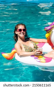 Caucasian Redhead Girl Having A Cocktail On A Floating Unicorn In A Swimming Pool. Summer Vibes. 