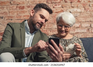 caucasian relatives son and elderly mother have a memory of past events while looking at his phone and printed pictures. High quality photo