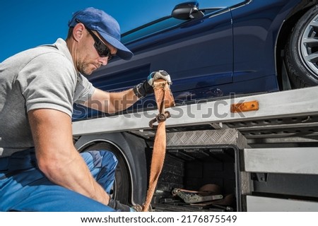 Caucasian Repo Company Worker in His 40s Securing Repossessed Vehicle on His Towing Truck. Automotive Car Loans Concept. 