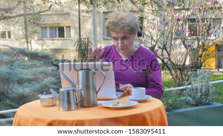 Caucasian retired woman using laptop relaxing in the garden for breakfast, having a videocall. Retirement, technology and relaxation concept.