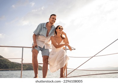 Caucasian romantic couple looking at beautiful view during yachting. Attractive young man and woman hanging out celebrating anniversary honeymoon trip while catamaran boat sailing during summer sunset - Powered by Shutterstock