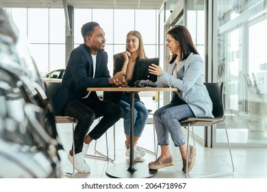 Caucasian saleswoman using digital tablet while working with multi ethnic couple at car salon. Happy man and woman talking with competent manager while buying auto. - Powered by Shutterstock