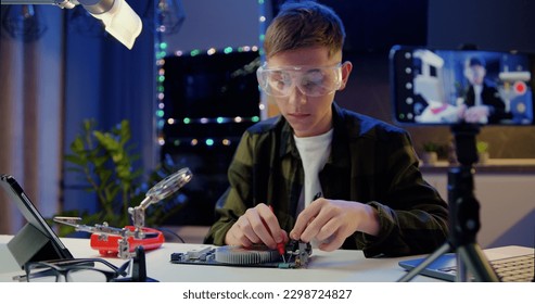 Caucasian schoolboy in glasses with a tool repairs a home electronic appliance. Male professional boy repairs a computer. Engineer soldering microcircuit. - Powered by Shutterstock