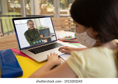 Caucasian schoolgirl wearing face mask using laptop on video call with male teacher. Online education staying at home in self isolation during quarantine lockdown.