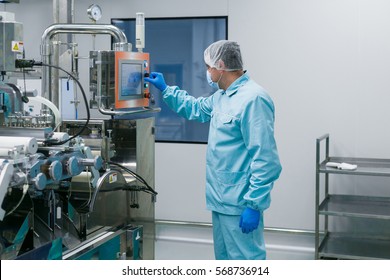 caucasian scientist in blue lab suit configures control panel in big clean room