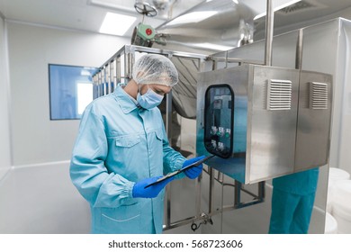 caucasian scientist in blue lab uniform stand near big steel machine with control panel, check readings