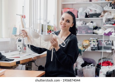caucasian Seamstress or dressmaker keeps bra or underwear in hands. Tailor making a garment in her workplace. looking at camera