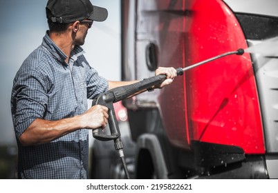 Caucasian Semi Truck Driver Washing His Vehicle Using Pressure Washer And Cleaning Detergent. Trucks Maintenance Theme.