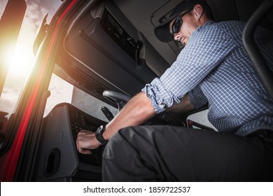 Caucasian Semi Truck Driver Wearing Black Baseball Hat Inside Vehicle Cabin Preparing To Hit The Road. Transportation And Cargo Industry Theme.