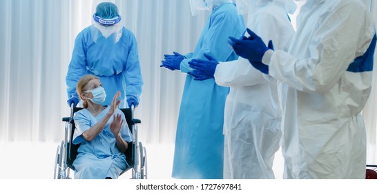 Caucasian Senior Coronavirus Covid-19 Infected Patient Sitting On Wheel Chair With Happy Doctor And Medical Team Ready To Send Her Back Home After Treatment And Recover From Desease At Hospital