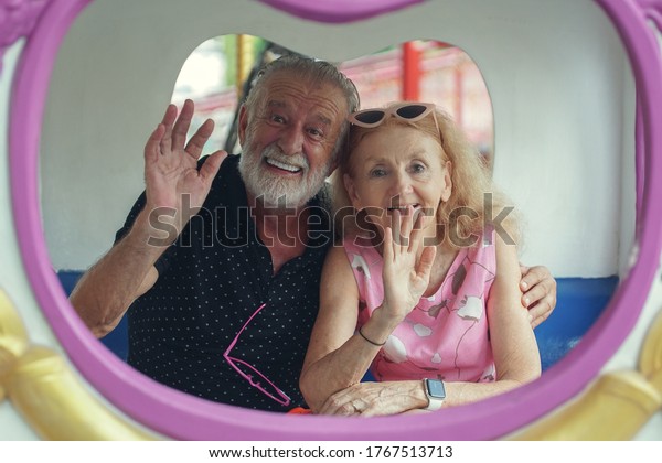 Caucasian Senior couples play and smile on merry go\
round at the amusement\
park