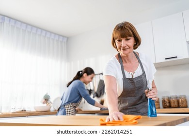 Caucasian senior elderly woman cleaning kitchen in house with daughter. Attractive female housekeeper and mature cleaner wear apron, feel happy and relax while working for housework or chores at home. - Powered by Shutterstock