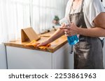 Caucasian senior elderly woman wearing apron, cleaning kitchen at home. Attractive mature old housekeeper cleaner feel tired and upset while wiping dining table for housekeeping housework or chores.
