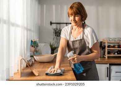 Caucasian senior elderly woman wearing apron, cleaning kitchen at home. Attractive mature old housekeeper cleaner feel tired and upset while wiping dining table for housekeeping housework or chores.
 - Powered by Shutterstock