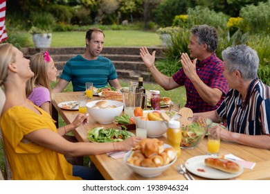 Un vieil homme caucasien assis à table parlant avec sa famille en train de manger dans le jardin. famille de trois générations célébrant le repas à l'extérieur ensemble.