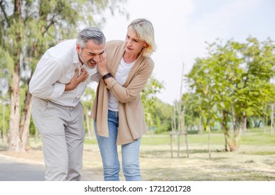 Caucasian senior man suffering, clutching and having chest pain cause from heart attack while walking in the park with his wife, older woman care and support husband, health problem and insurance 